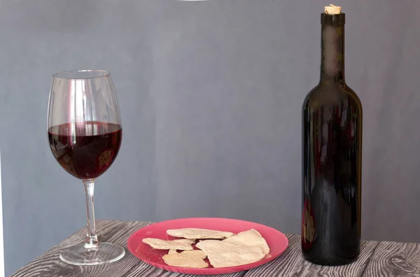 A glass of dry red wine and unleavened bread on a plate. Nearby is a bottle of wine. On brushed pine boards. On a gray background. Celebration of the Lord's Supper.