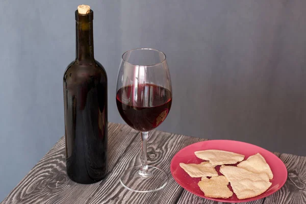 A glass of dry red wine and unleavened bread on a plate. Nearby is a bottle of wine. On brushed pine boards. On a gray background. Celebration of the Lord's Supper.