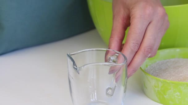 Une femme verse un verre d'eau de carafe. Près du récipient avec de la farine. Gros plan . — Video