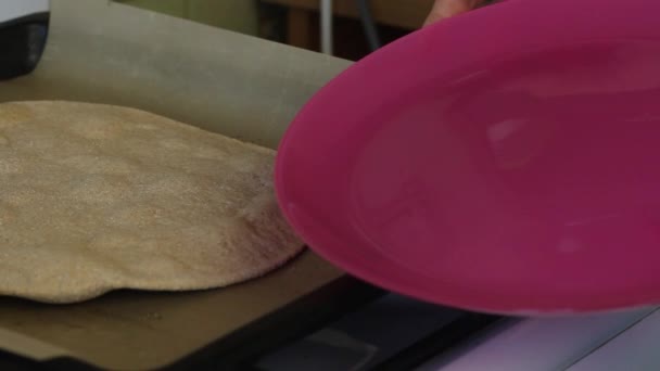 Een vrouw schuift een gebakken ronde taart van een bakplaat naar een bord. Bereid een verse tortilla voor. — Stockvideo