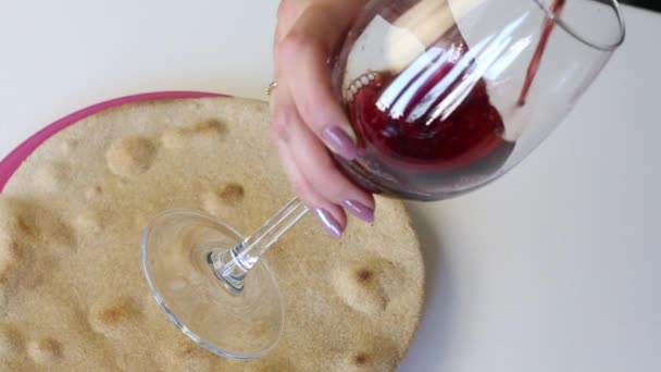 Sul tavolo c'è un piatto con una torta fresca rotonda al forno. Sopra di lei, una donna tiene un bicchiere e vi versa del vino rosso. Lo mette su una vanga con una tortilla . — Video Stock