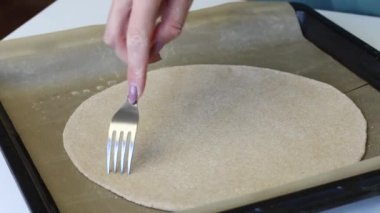 Bir kadın yuvarlak hamurlu keki çatalla deliyor. Elinde silikon bir minderle bir yemek tepsisinin üzerinde yatıyor. Taze bir tortilla hazırlar..