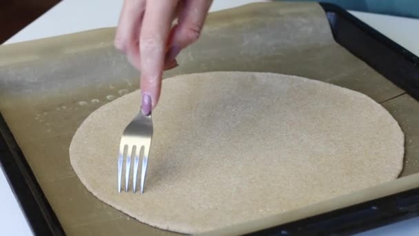 Eine Frau durchbohrt mit einer Gabel einen runden Teigkuchen. Sie liegt auf einem Backblech mit Silikonmatte. Bereitet eine frische Tortilla zu. — Stockvideo