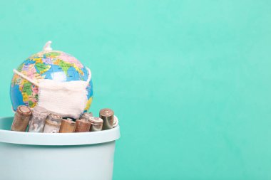 Çöpte aşınmayla kaplanmış, kullanılmış parmak tipi piller. Onlar çöp tenekesinde sargı bezli bir küre. Çevre koruma, Dünya Günü. Yeşil bir arkaplanda.