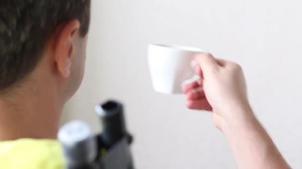 Ein Mann sitzt mit dem Rücken zur Kamera und trinkt Kaffee aus einem Becher. Nahaufnahme. — Stockvideo