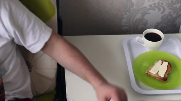 Bir adam tepsiden bir kupa kahve alır. Yakınlarda bir tabakta tereyağlı bir tost var.. — Stok video