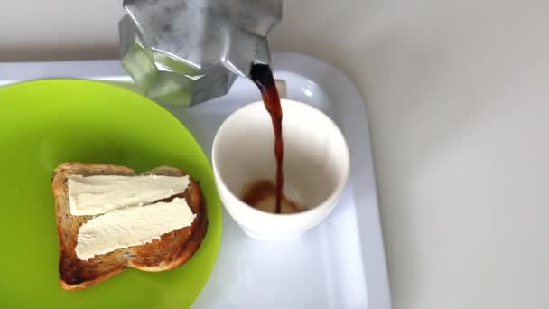 Een man schenkt koffie in een mok. Vlakbij op een bord ligt een toast waarop boter wordt gelegd. Close-up opname. — Stockvideo