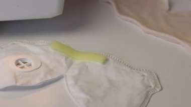 Kadın, kumaştan yapılmış koruyucu bir maske ve eldivenler dikiyor. Dikiş makinesinde. Eldiven deniyorum. Masada dikilmiş bir maske var. Evde çalış..