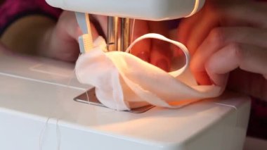 Bir kadın kumaştan koruyucu bir maske dikiyor. Dikiş makinesinde. Evde çalış..