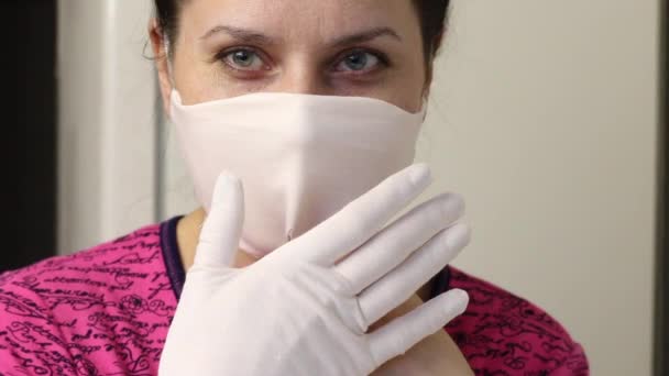 Kvinnan syr en skyddande mask och handskar av tyg. På en symaskin. Försöker med mask och handskar. Arbete i hemmet. — Stockvideo