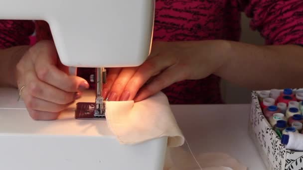 Donna cuce su una macchina da scrivere una maschera protettiva fatta di stoffa. Accanto al tavolo ci sono fili e strumenti. Lavoro a casa . — Video Stock