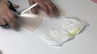 Bir adam kumaştan koruyucu bir maske yapar. Kesik kumaşı şablonla karşılaştırır. Evde çalış..