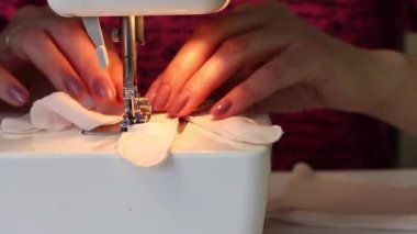 Kadın kumaştan eldiven dikiyor. Dikiş makinesinde. İğne tutacağı ve ayağı yakın plan çekilecek. Evde çalış..