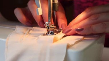 Kadın kumaştan eldiven dikiyor. Dikiş makinesinde. İğne tutacağı ve ayağı yakın plan çekilecek. Evde çalış.