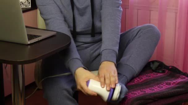 A man works at a laptop in isolation, at home. He takes a break, massages the calf muscles and feet with an electric massager — Stock Video