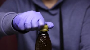 Lastik eldivenli genç bir adam bir şişe biranın mantarını kapatıyor. Kendini izolasyonda boş zaman.