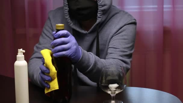 En ung man i skyddsmask och gummihandskar torkar en flaska öl med en servett och skruvar loss korken. Fritid i självisolering. — Stockvideo