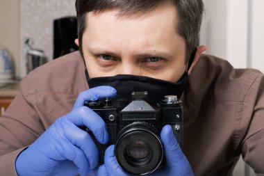 Lastik eldivenli ve maskeli bir adam önünde bir kamera tutuyor. Uzağa doğru bakıyor. Kendini izole eden fotoğrafçı..