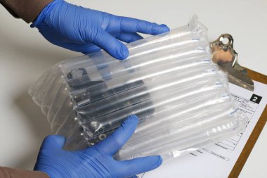 Kendini tecrit sırasında paket teslimatı. Lastik eldivenli bir adam, içinde kamera olan bir balon çanta tutuyor. Teslimat formunun yanında..