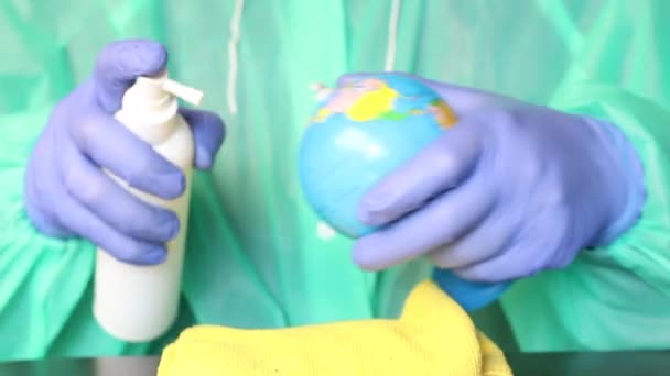 Een man met rubberen handschoenen en een beschermende jas behandelt de wereld met een ontsmettingsmiddel. De planeet schoon houden is de tijd van de epidemie. — Stockvideo