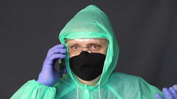 Un hombre con guantes de goma, impermeable y gafas está hablando por teléfono. Gestos profundos durante una conversación . — Vídeo de stock
