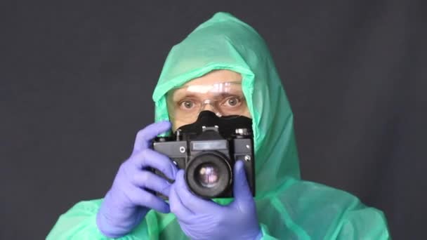 Fotograf w gumowych rękawiczkach, płaszczu przeciwdeszczowym i okularach zdejmuje pokrywę z kamery i rozpoczyna fotografowanie. — Wideo stockowe