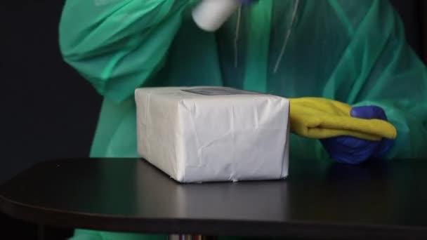 Livraison de correspondance pendant une pandémie. Un homme en gants de caoutchouc et un imperméable traite le colis reçu avec un antiseptique et l'essuie avec une serviette. Symbole de la lutte contre la pandémie — Video