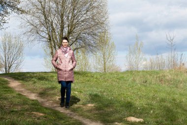 Bir kız bahar parkında yürüyor. Bahar ceketi giymişti, boynunda bir atkı vardı. Ağaçların üzerinde çiçek açan yeşilliklerin etrafında.