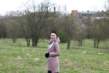 Bir bahar parkında gülümseyen bir kızın portresi. Bahar ceketi giymişti, boynunda bir atkı vardı. Yeşillik yaprakları ağaçlarda görülebilir..