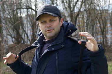 Genç bir adam bahar parkında yürüyor. Omuzlarındaki sırt çantasını düzeltiyor. Bahar ceketi giymişti, şapkası kafasındaydı. Temiz havada yürü..