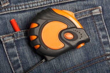 Arka cebinde turuncu ve siyah elementlerin asılı olduğu bir mezura var. Yakınlarda kırmızı bir kalem var. İşçi Bayramı 'nın sembolü.