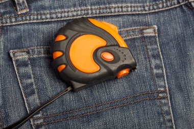 Arka cebinde turuncu ve siyah elementlerin asılı olduğu bir mezura var. İşçi Bayramı 'nın sembolü.