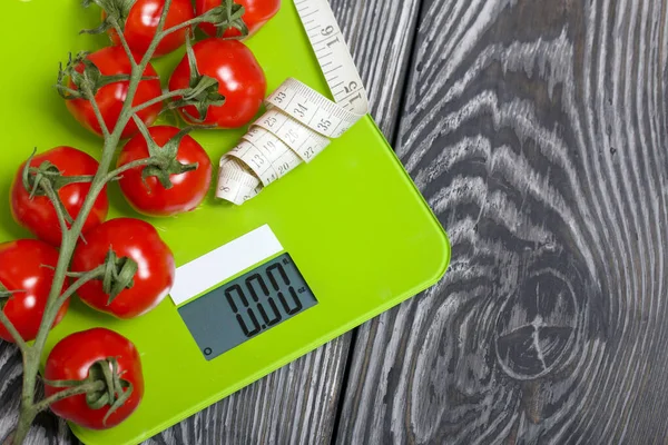 Bunches of tomatoes are on the scales. Near the measuring tape. On brushed pine boards. Symbol of World No Diet Day.