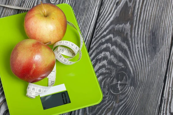 Apples and a measuring tape lie on the scales. Scales show zero. On brushed pine boards. Symbol of World No Diet Day.