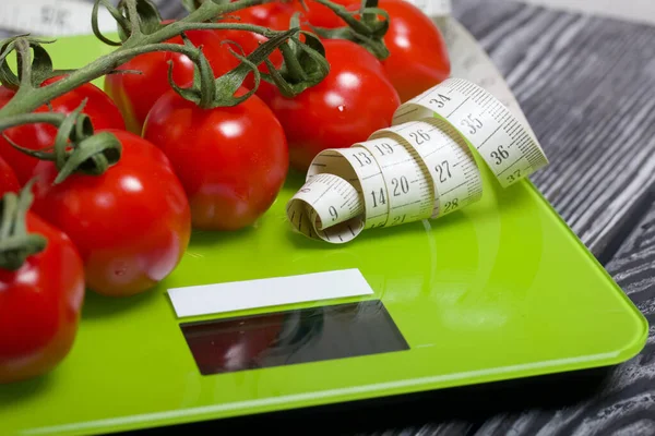 Bunches of tomatoes are on the scales. Near the measuring tape. On brushed pine boards. Symbol of World No Diet Day.