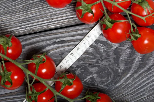 Bunches of tomatoes. Near the measuring tape. On brushed pine boards. Symbol of World No Diet Day.