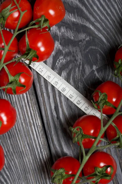 Bunches of tomatoes. Near the measuring tape. On brushed pine boards. Symbol of World No Diet Day.