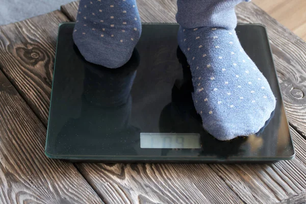 A man is standing on the floor scales. The scales stand on black brushed pine boards. Legs taken up close up.