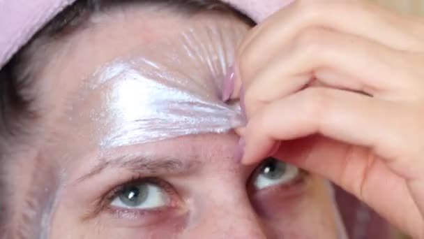 Una mujer se quita una máscara de papel de aluminio cosmético plateado con plata coloidal de su cara. Cuidado de la piel problemática. La parte superior de la cara de una mujer se dispara de cerca . — Vídeos de Stock