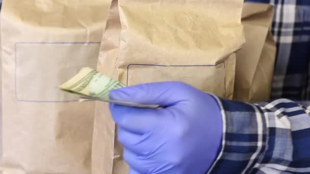 Sacs en papier avec nourriture. Un homme en gants de caoutchouc tient des billets en dollars dans ses mains, paie la commande. Livraison à domicile pendant une épidémie . — Video