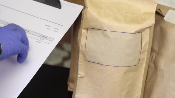 Człowiek w gumowych rękawiczkach patrzy przez wypełniony formularz dostawy i stawia na niego dolary. Potem odbiera jedzenie w papierowych torbach. Dostawa żywności w czasie epidemii. — Wideo stockowe