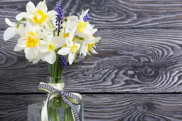 Bouquet of spring flowers in a bottle. Ordinary and terry daffodils. A ribbon bow is tied to the neck of the bottle. Against the background of brushed boards painted black.