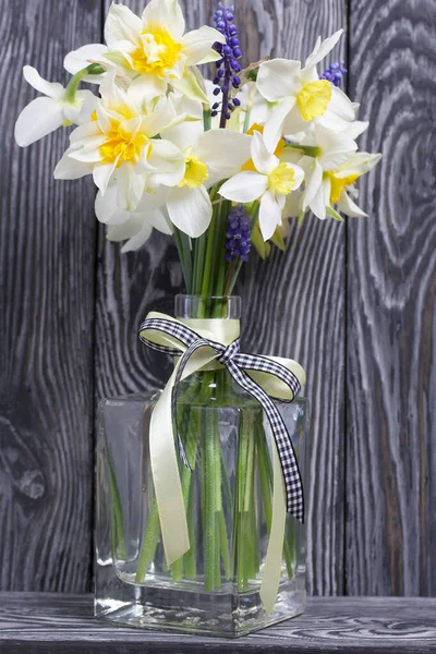 Bouquet of spring flowers in a bottle. Ordinary and terry daffodils. A ribbon bow is tied to the neck of the bottle. Against the background of brushed boards painted black.