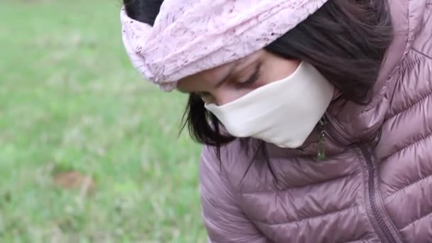 En flicka i skyddsmask sliter av en påsklilja som växer på en våräng. Samlar en bukett. Närbild skott. Gå i friska luften under en epidemi. — Stockvideo