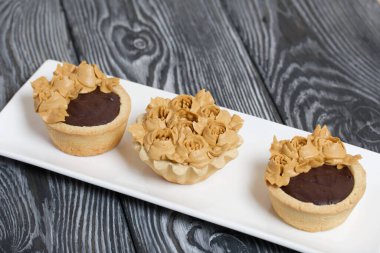 Çikolatalı ganache turtaları ve kekler. Krem şantili çiçeklerle süslenmiş. Kremanın karamel rengi var. Fırçalanmış çam ağaçlarında siyaha boyanmış.