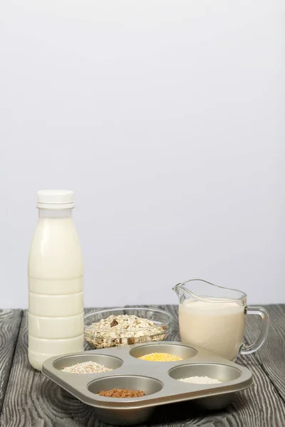 Bottle and glass with milk. Nearby in the container are cereals: buckwheat, rice, corn, barley and oatmeal. On brushed pine boards.