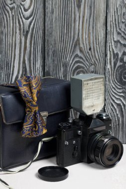 Fotoğrafçı aksesuarları. Kamera ve flaş. Kamerada bir papyon var. Fırçalanmış çam ağaçlarının arka planında.
