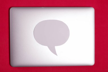 Kapağı kapalı bir blog dizüstü bilgisayar. Kapağında bir konuşma balonu var. Mercan renginin arka planına karşı.