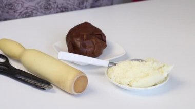 Masanın üzerinde kahverengi bir hamur ve hindistan cevizi var. Tatlı malzemeleri ve aletler. Kadınlar filmlere sarılır..