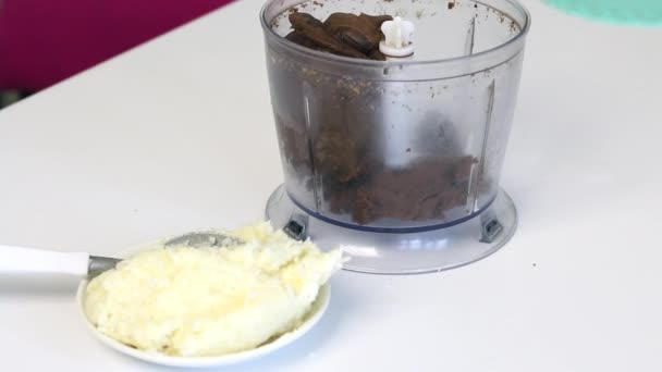 Em uma tigela de liquidificador encontra-se um pedaço marrom de massa e chocolate para fazer uma sobremesa. Perto de flocos de coco — Vídeo de Stock